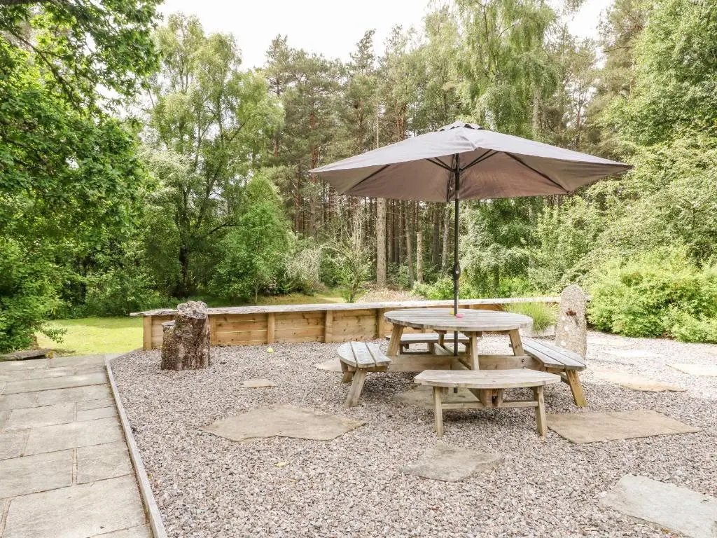 a picnic table and bench with an umbrella at Tigh Na Drochit in Garve