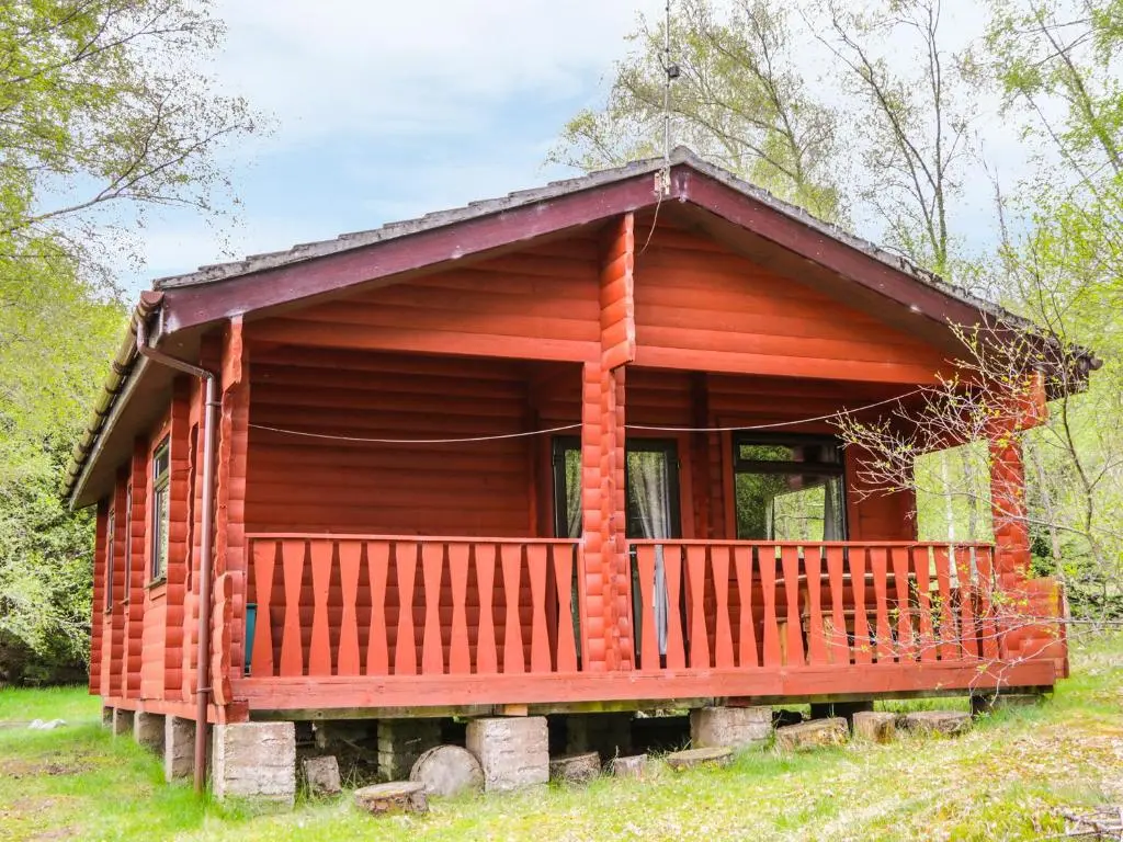a small log cabin with a porch in a field at Otter Lodge in Strathpeffer