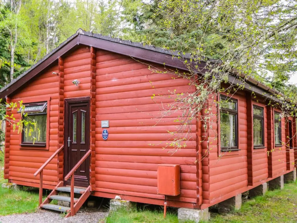 a red cabin with a staircase in a forest at Otter Lodge in Strathpeffer