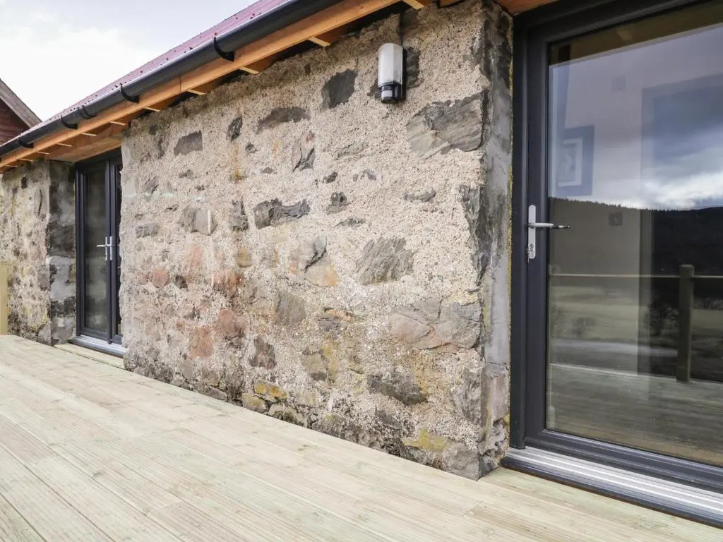 a brick wall with a window and a wooden deck at East Craigdhu Cow Byre in Beauly