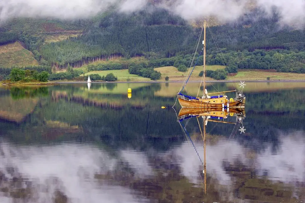 a boat on a lake with its reflection in the water at The Bridge Suite in Invermoriston