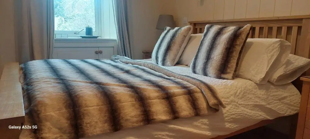 a bed with a blanket and pillows on it at Fairdene Cottage in Ballater