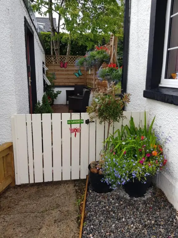 a fence in front of a house with flowers at Nanny's little highland hoose in Inverness