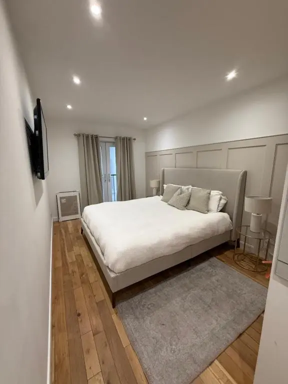 a white bedroom with a large white bed and a television at Gateway Apartment in Inverness