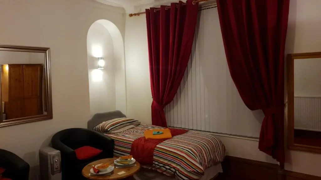 a small room with a table and a chair and red curtains at Broomlea Guest House in Dyce