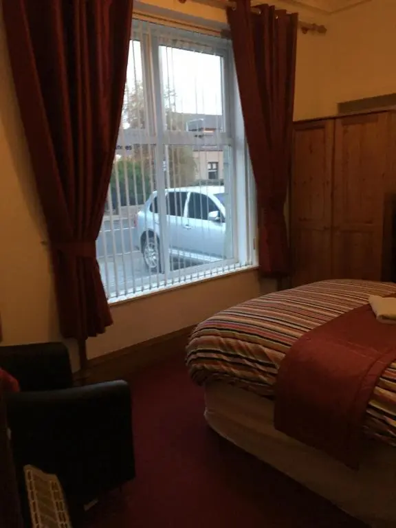 a bedroom with a bed and a window with a car outside at Broomlea Guest House in Dyce