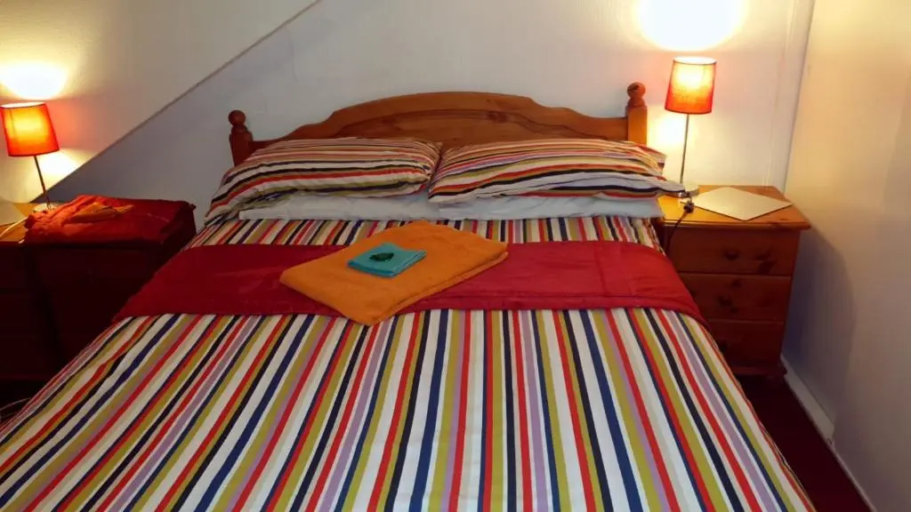 a bed with a colorful striped blanket and two lamps at Broomlea Guest House in Dyce