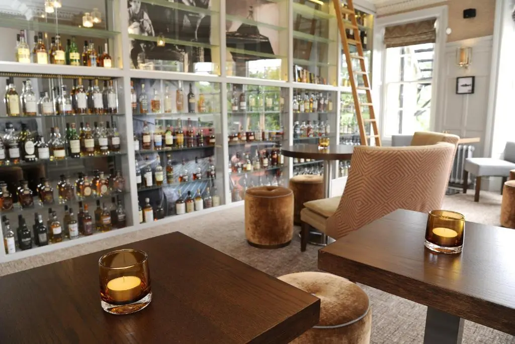 a bar with two tables and shelves of alcohol at The Dowans Hotel of Speyside in Aberlour