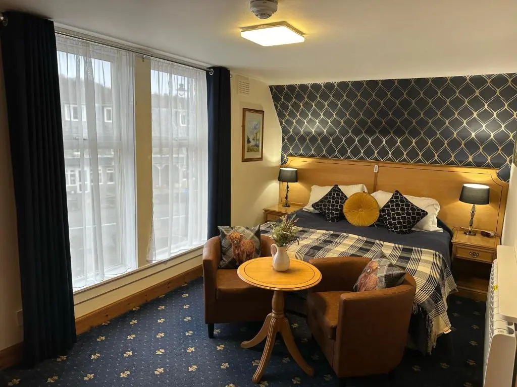 a hotel room with a bed and a table and chairs at The Glen Hotel Newtonmore - Rooms, bar & restaurant in Newtonmore