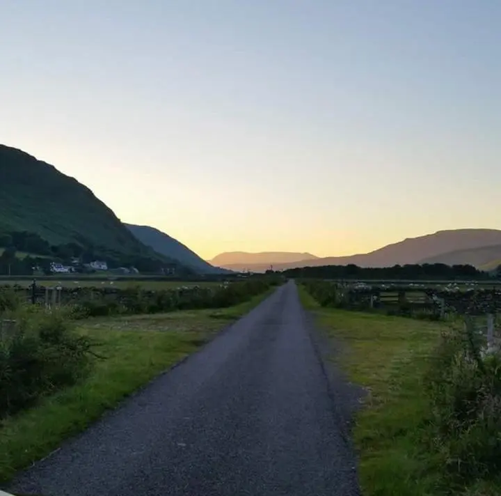 a road leading into a field with mountains in the distance at Clachan Farmhouse B & B in Ullapool