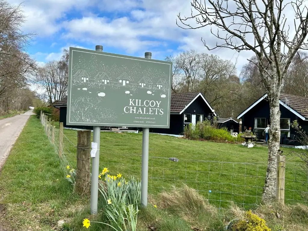 a sign in front of a yard with a house at Kilcoy Chalets in Muir of Ord