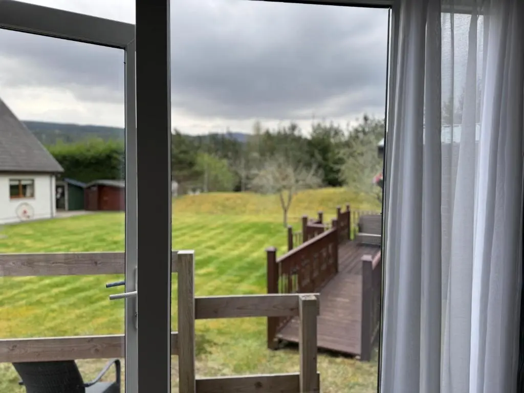 a window with a view of a yard and a deck at The Garden Room Tiny House Bed and Breakfast Stay in Glenmoriston