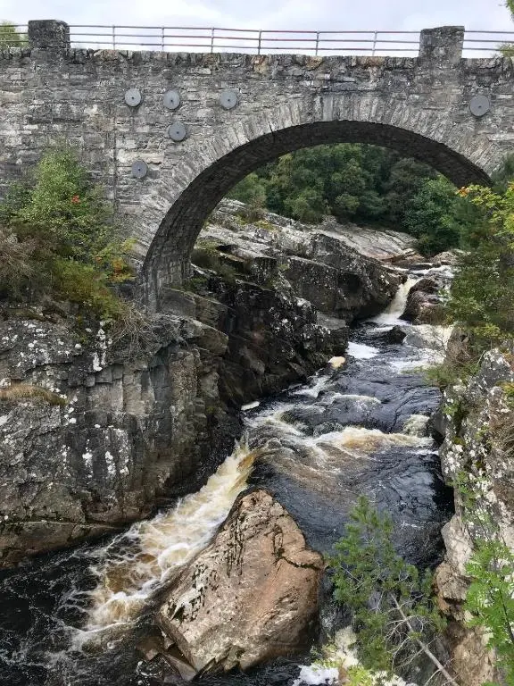 a stone bridge over a stream with a train crossing it at Rosemount Bothy - Highland Cottage in Garve