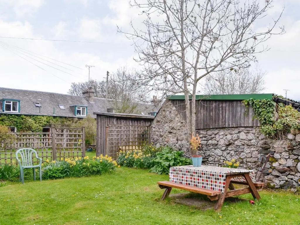 a garden with a table and a stone wall at Larch Cottage in Balnald