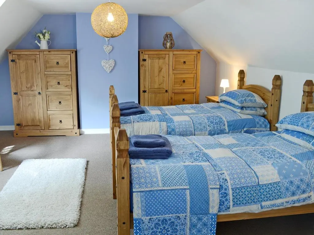 two beds in a bedroom with blue walls at Garden Cottage in Tain