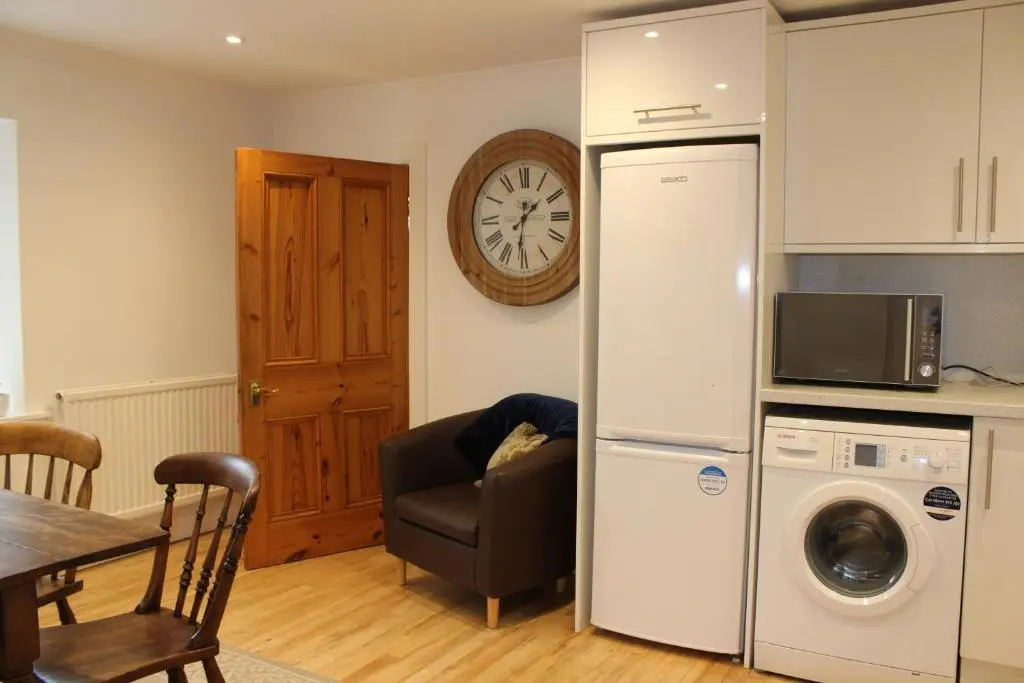 a kitchen with a refrigerator and a table with a chair at Ceol Na Mara Cottage by the sea in Nairn
