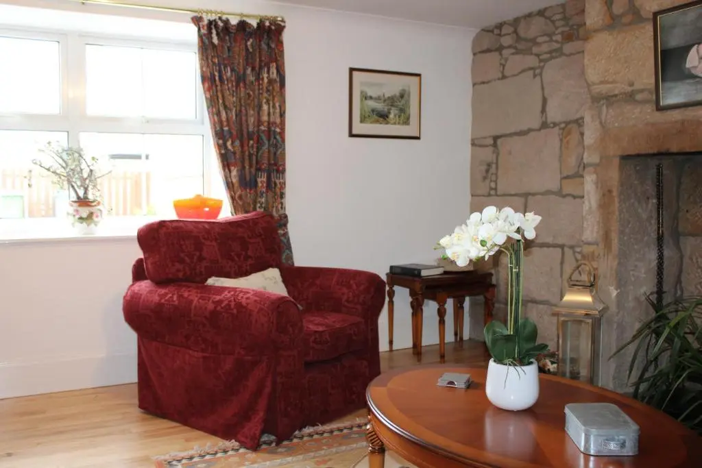 a living room with a red chair and a table at Ceol Na Mara Cottage by the sea in Nairn