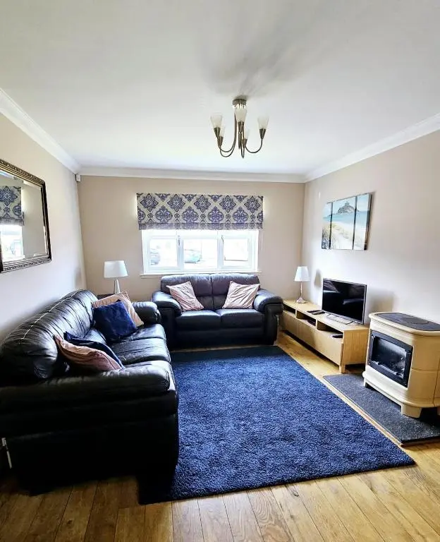 a living room with a leather couch and a blue rug at 26 Woodgrove Drive in Inverness