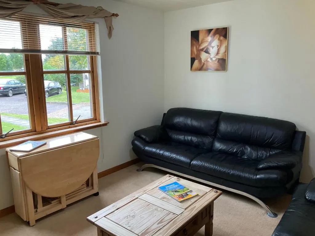a living room with a black leather couch and a table at Two Bedroom Glen View Free Parking in Inverness