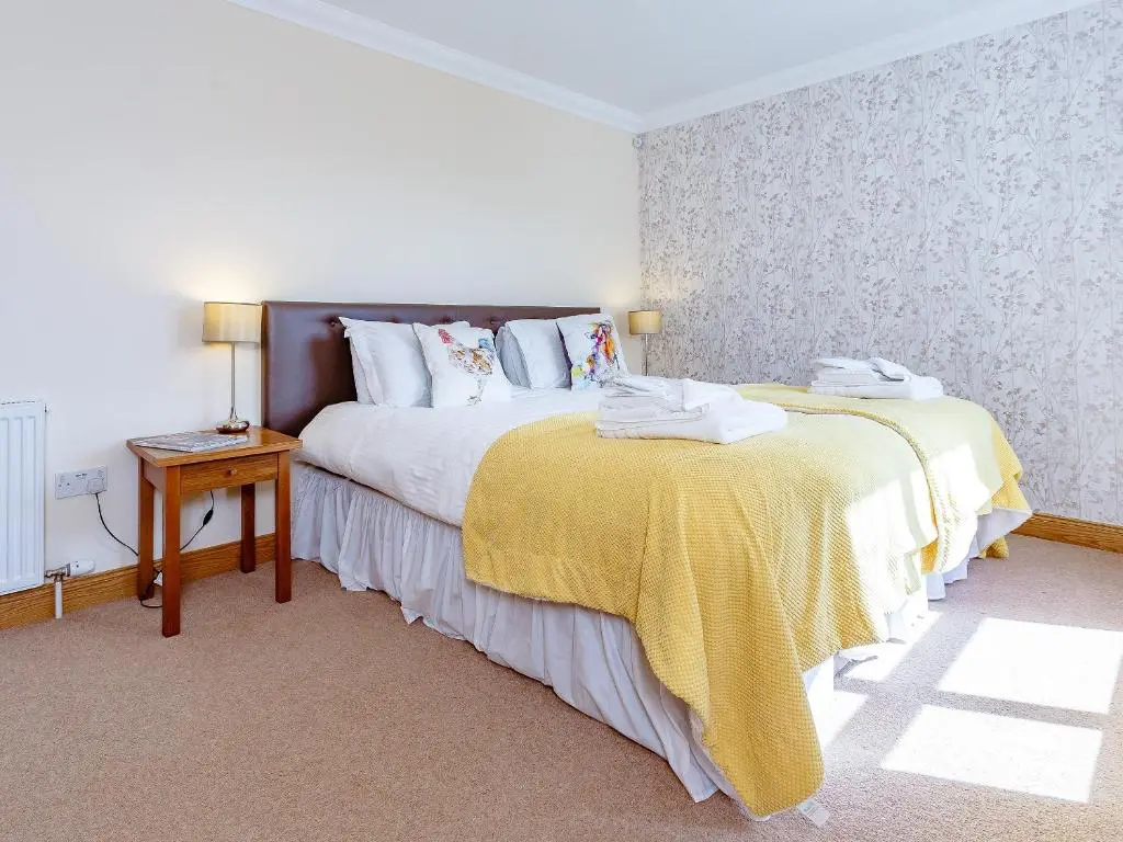 a bedroom with a bed with a yellow blanket and a table at The Lookout in Aviemore