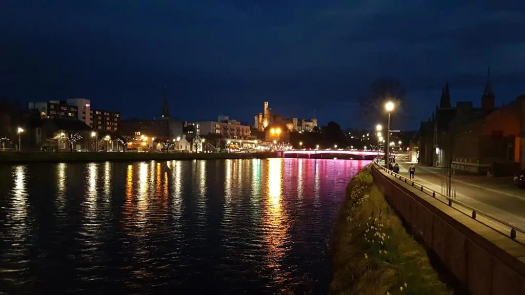 a city lit up at night with a body of water at 37 Farraline Court, City Centre apartment in Inverness