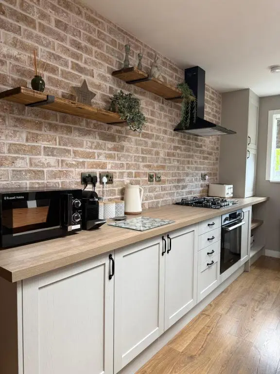 a kitchen with white cabinets and a brick wall at Wells Street Cottages No 26 By The River Ness in Inverness