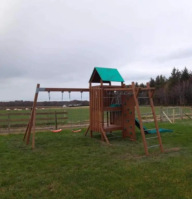 a playground with a wooden play structure in a field at Greencraig Pods in Buckie