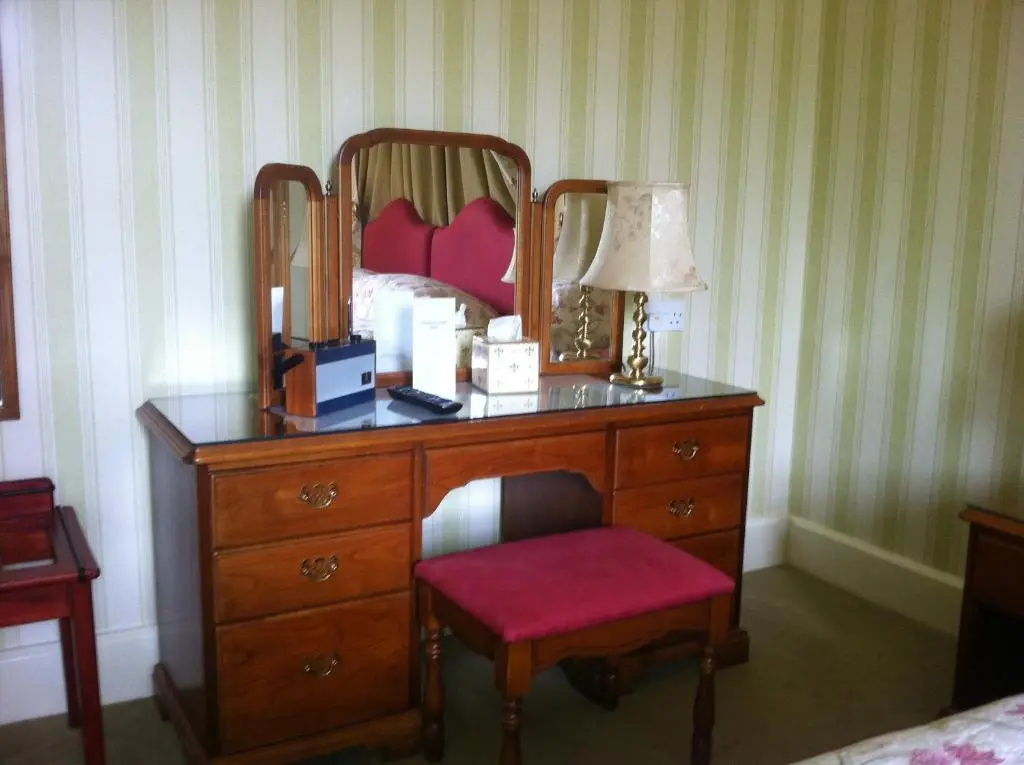 a bedroom with a dresser with a mirror and a chair at Glengarry Castle Hotel in Invergarry