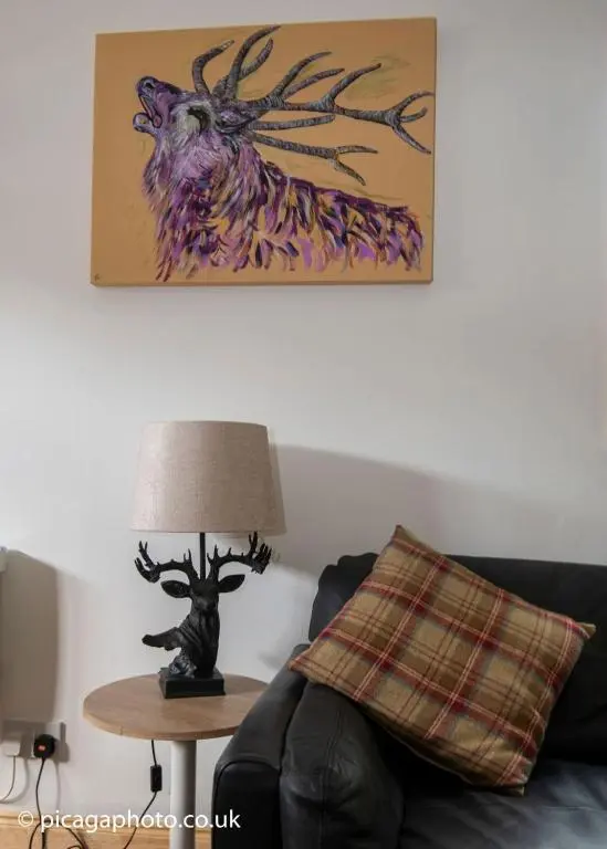 a living room with a couch and a table with a lamp at Loch Ness Studio Blairbeg in Drumnadrochit