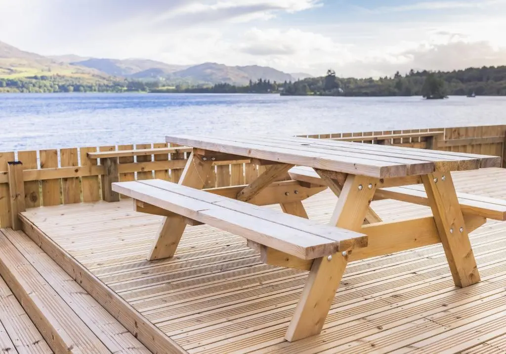 a wooden picnic table sitting on a dock next to the water at Loch Ness Cottage in Fort Augustus