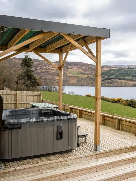 a hot tub on a deck next to a lake at Loch Ness Cottage in Fort Augustus