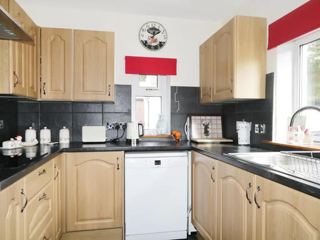 a kitchen with wooden cabinets and a white dishwasher at St Aethans in Inveran