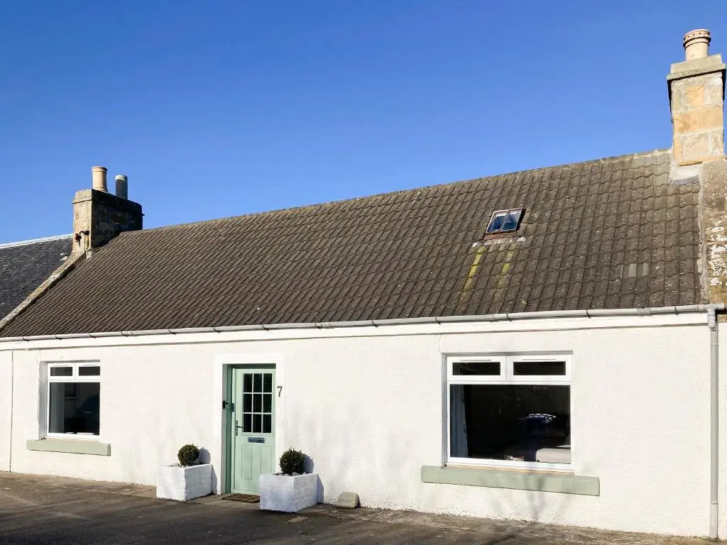 a white building with a brown roof and two windows at Fisher's Cottage in Balintore