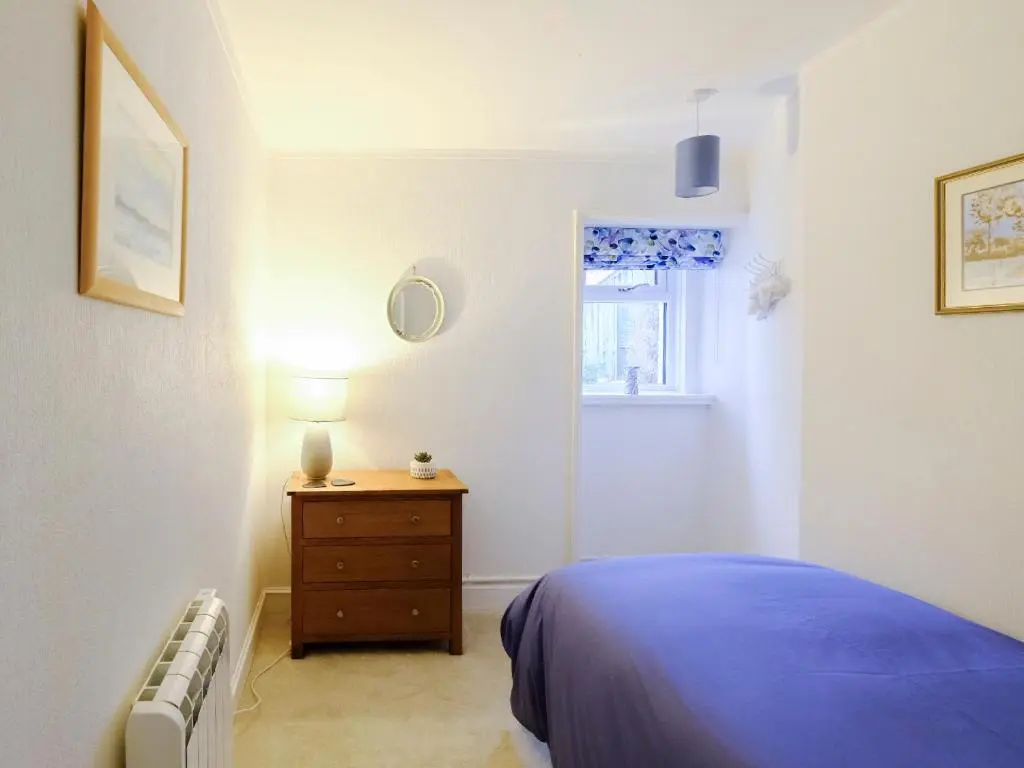 a bedroom with a bed and a dresser and a window at Fisher's Cottage in Balintore
