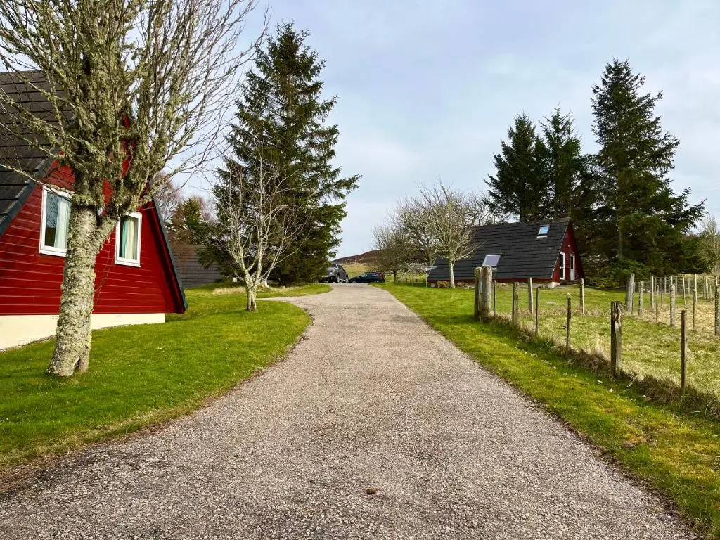 a gravel road next to a red barn and trees at Highland Glen Lodges in Rogart