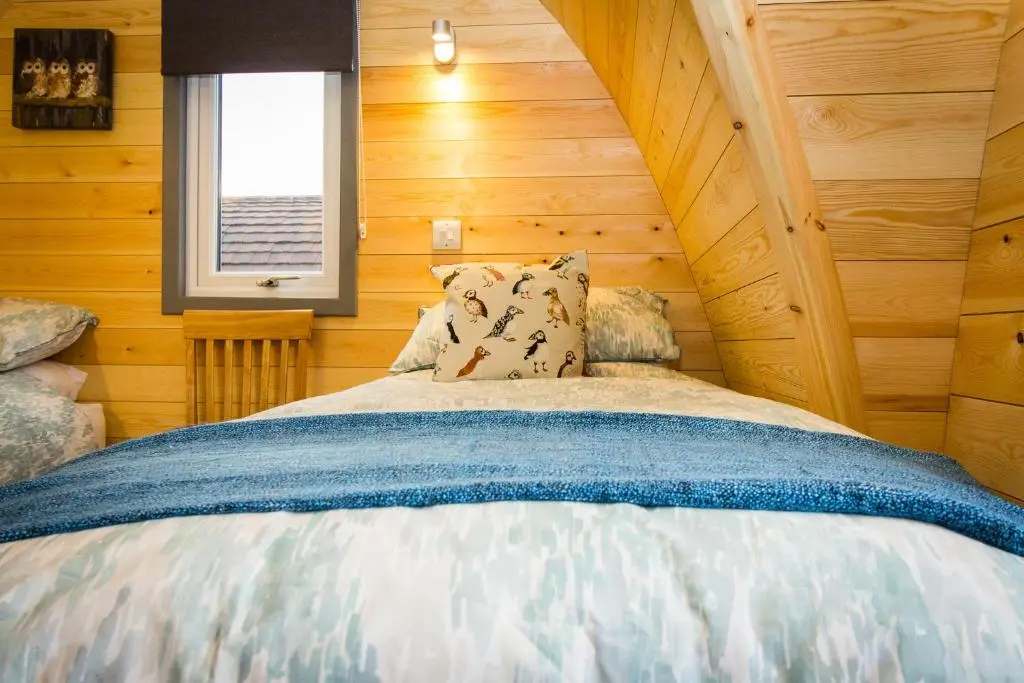 a bed in a room with wooden walls and a window at Evelix Pods Dornoch in Dornoch