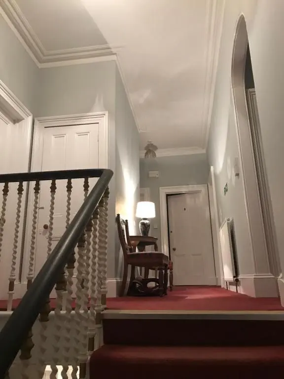 a hallway with a staircase with a chair and a lamp at Park Guest House in Inverness