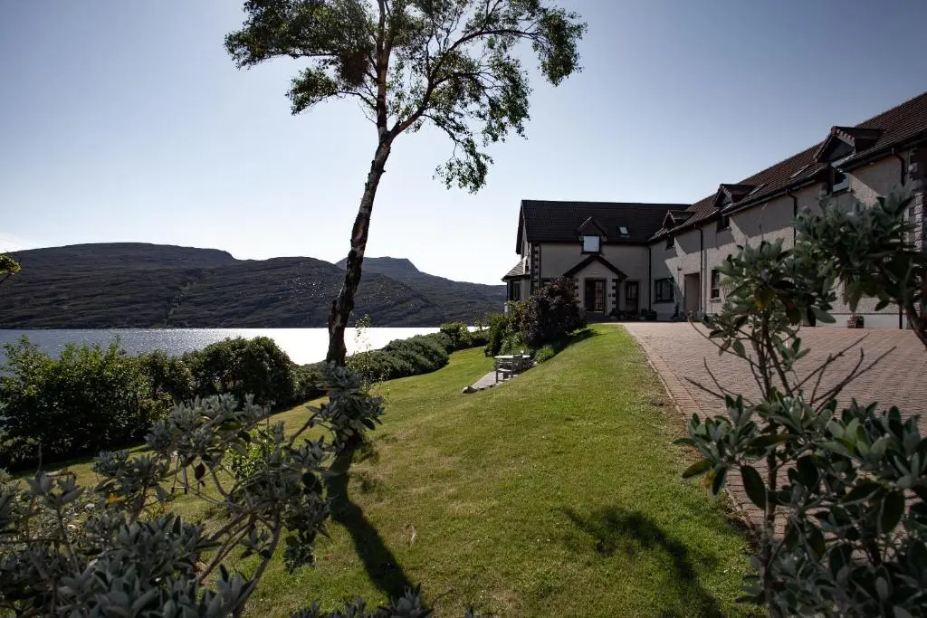 a house with a tree next to a body of water at Ardvreck House in Ullapool