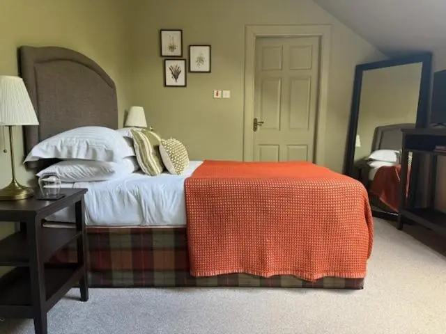 a bedroom with a bed with an orange blanket on it at Ardvreck House in Ullapool