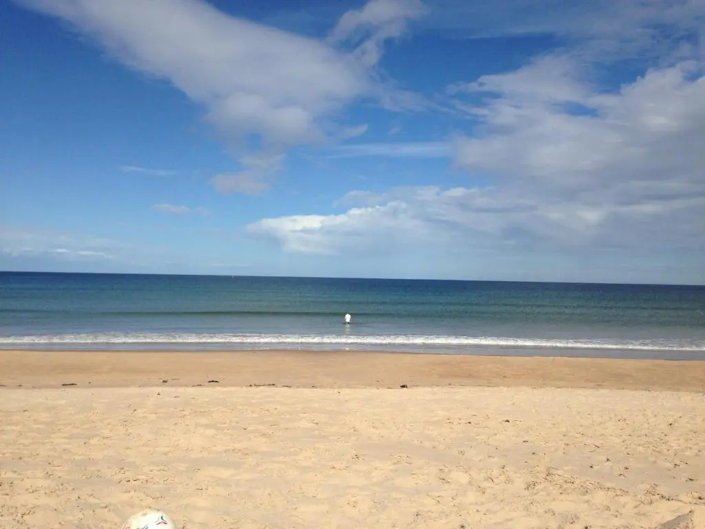 a beach with a person standing in the ocean at 3 Marina Quay in Lossiemouth