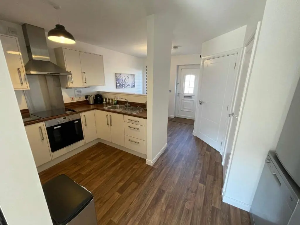 a kitchen with white cabinets and a wooden floor at Gorsebank View in Inverness