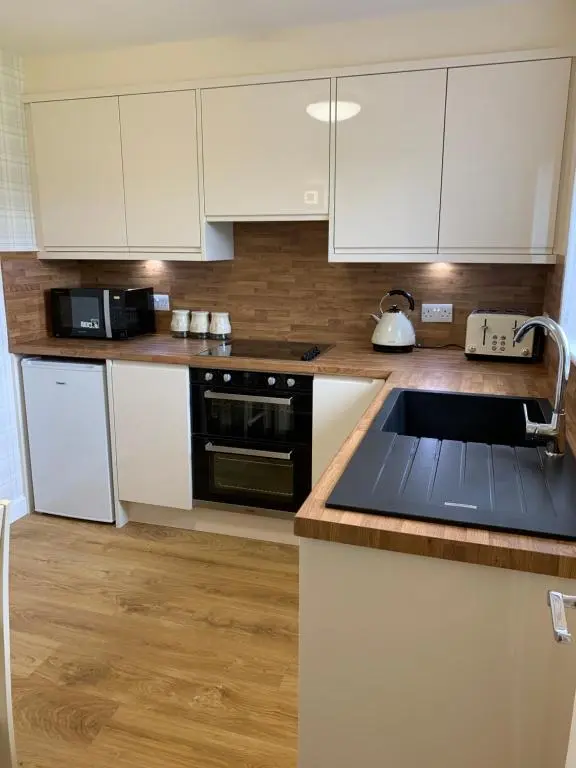 a kitchen with white cabinets and a sink at Greenfield Cottage in Thrumster