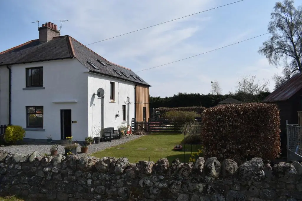 a white house with a stone fence in front of it at Lycia Rooms + in Inverness