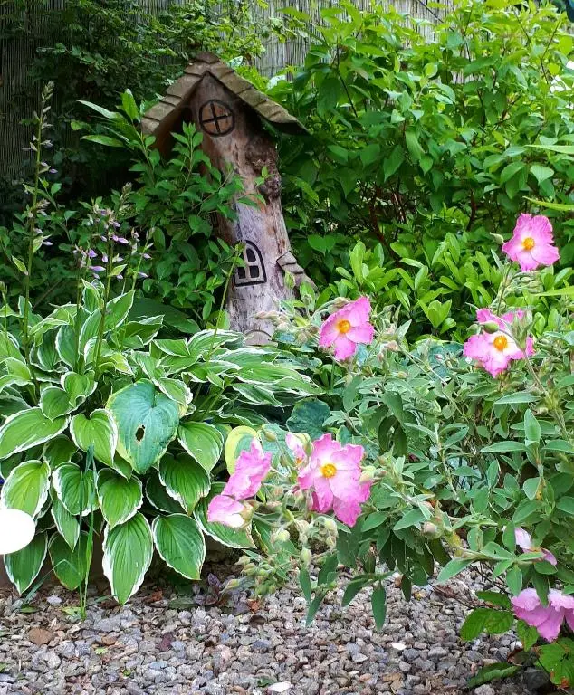 a garden with a bird house and pink flowers at Lycia Rooms + in Inverness