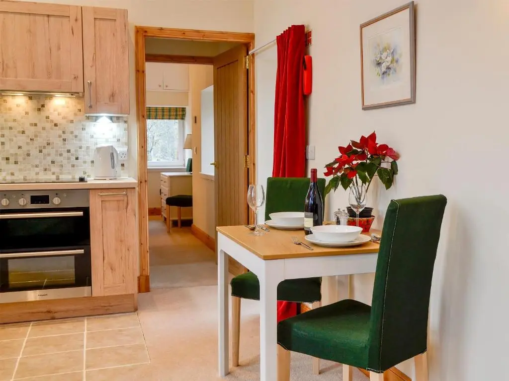 a kitchen with a table and green chairs at The Old Inverchroskie Kennels in Enochdhu