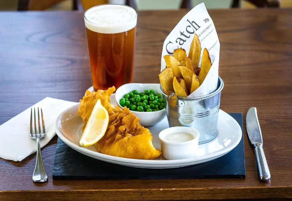 a plate of food with a drink and chips and peas at The Bandstand in Nairn