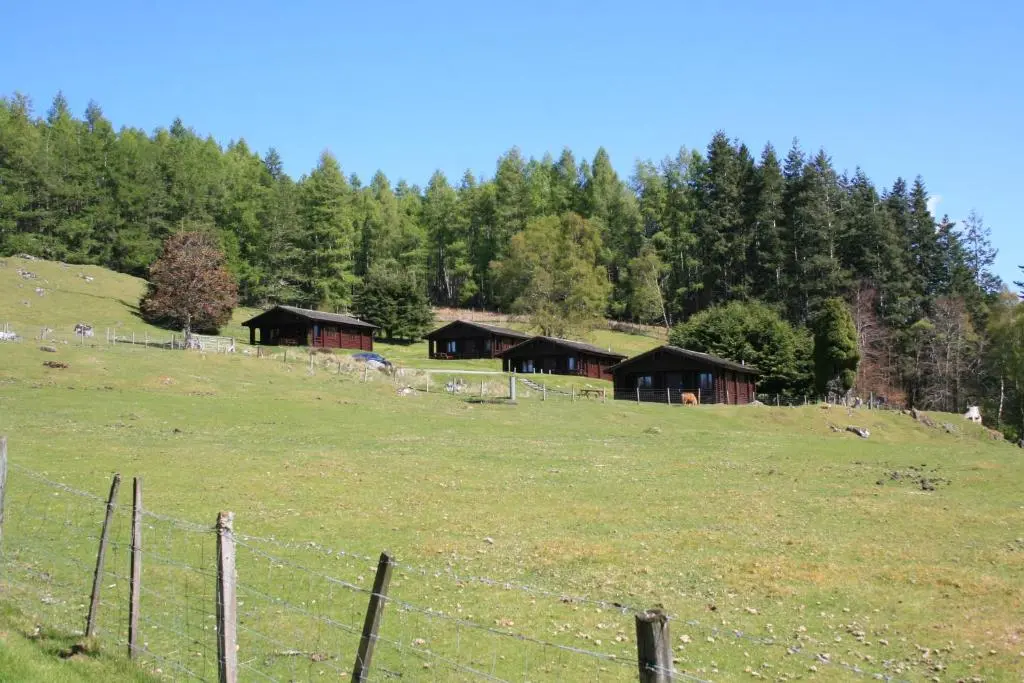 a field with a fence and buildings on a hill at Highgarry Lodges in Invergarry