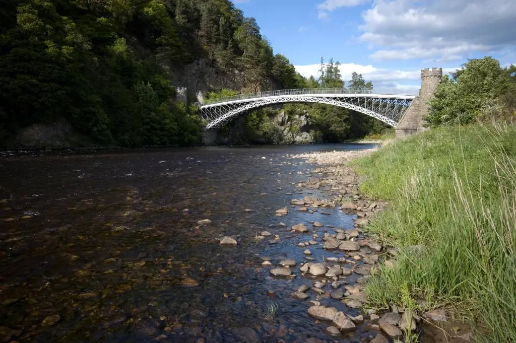 a white bridge over a river with rocks and trees at Dandaleith Cottage No.1 in Craigellachie