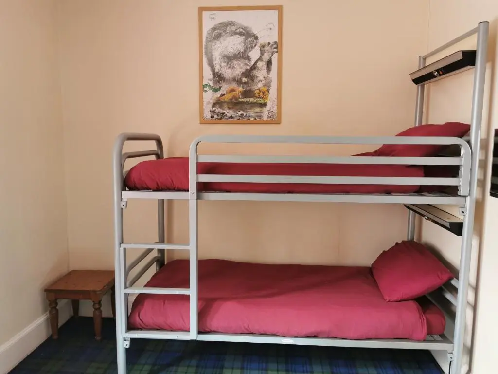 a room with three bunk beds with red pillows at Morag's Lodge in Fort Augustus
