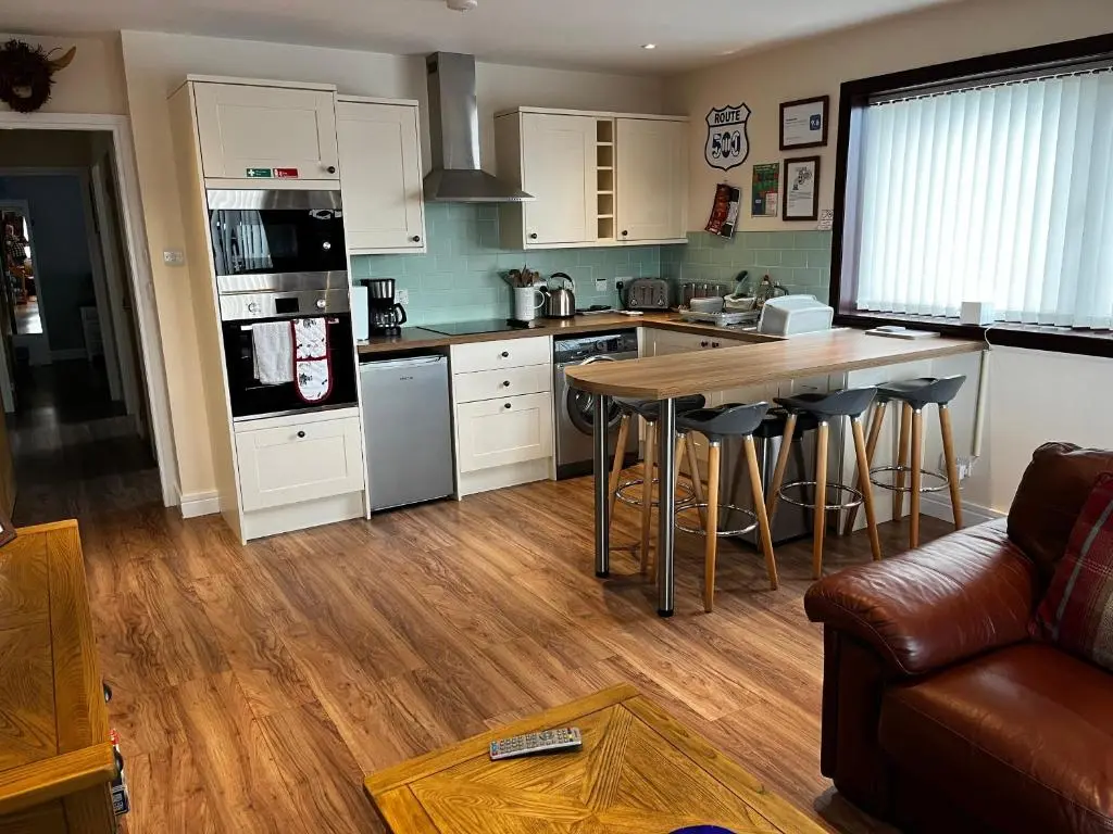a kitchen with white cabinets and a wooden floor at Lesanne Cottage in Inverness